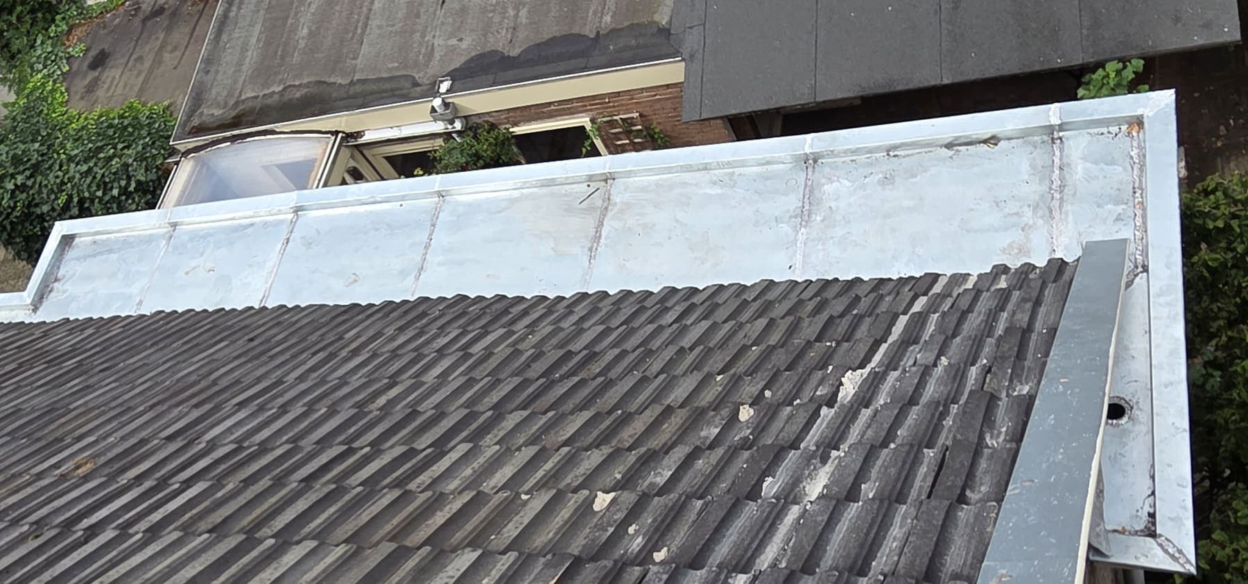 Nieuwe zinken bakgoot langs een pannendak, strak op maat gezet