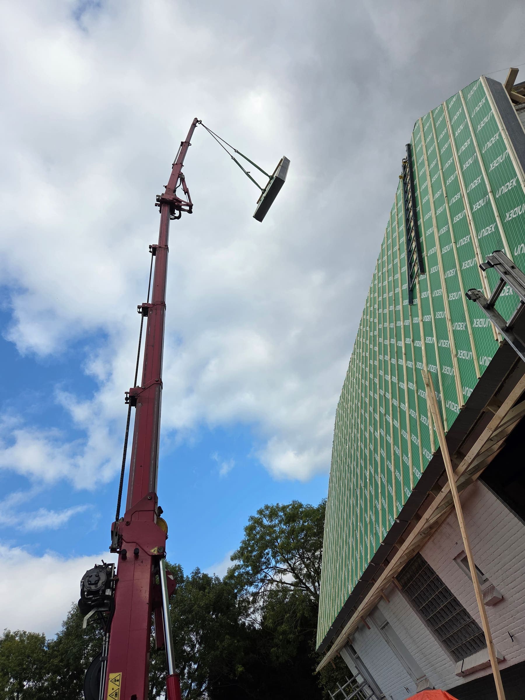Een kraan tilt materiaal op het dak; de groene renovatieplaten liggen er al op